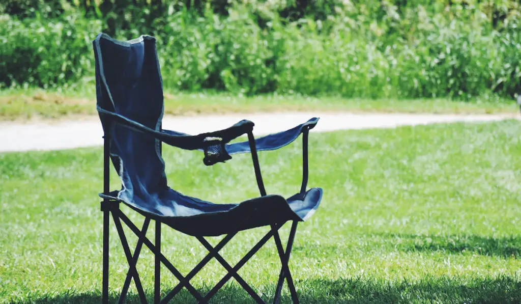An empty lonely camping foldable lawn chair standing in a shade under a tree
