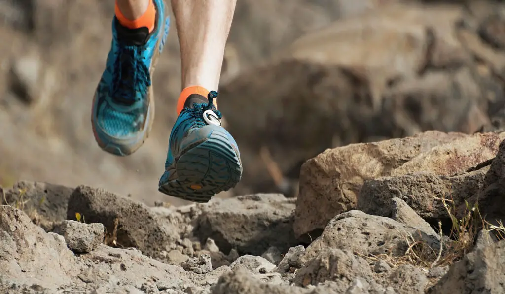 Athlete trail running in the mountains on rocky terrain, trail running shoes detail 