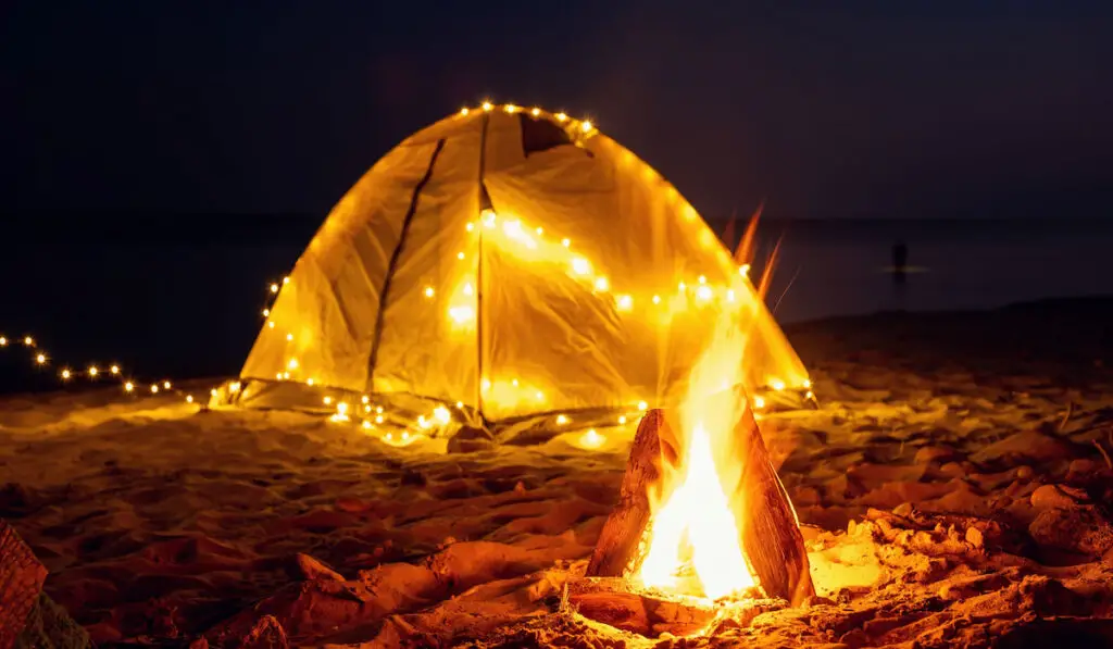 Camping on the beach. Campfire and tent with yellow lights on sea shore