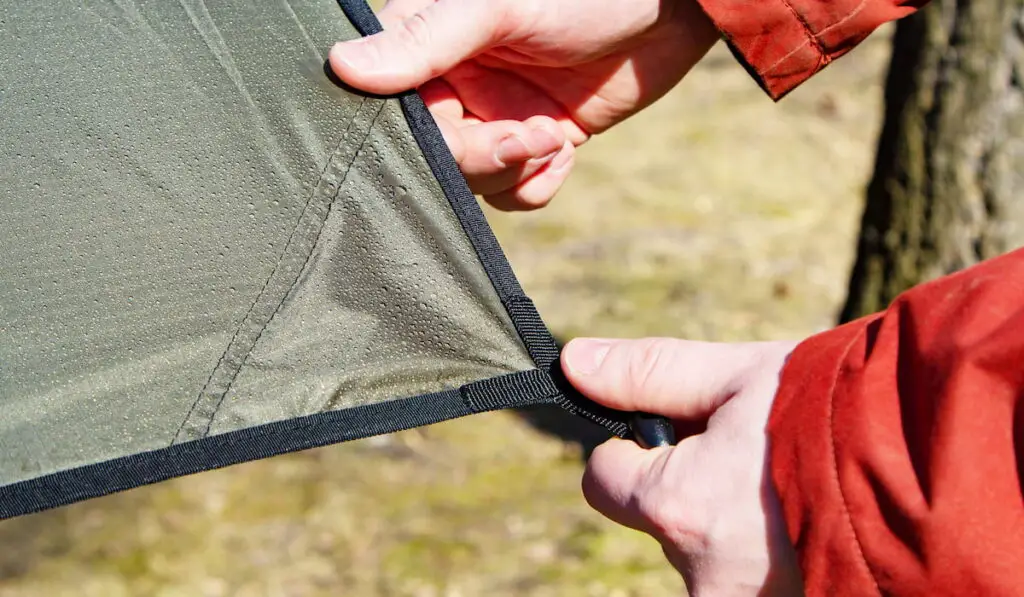 Close-up of male hands and the corner of an tarp with a grommet