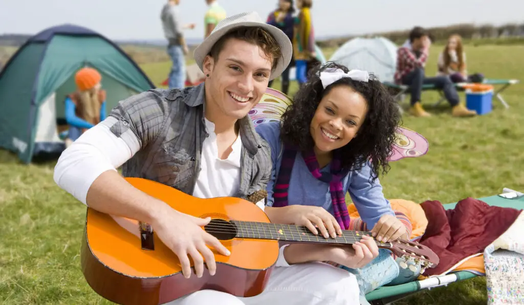 Couple with guitar sitting on a cot camping with their friends 
