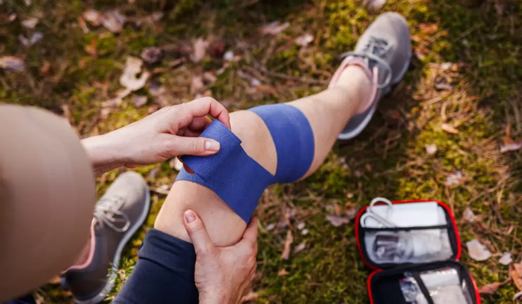 Injured woman using elastic bandage from first aid kit during hiking