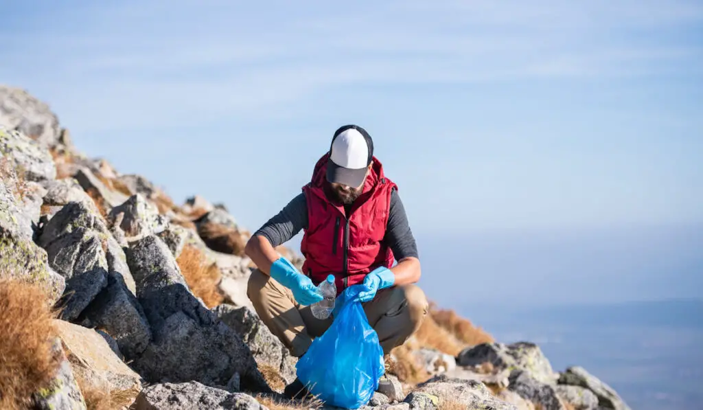 Man hiker picking up litter in nature in mountain