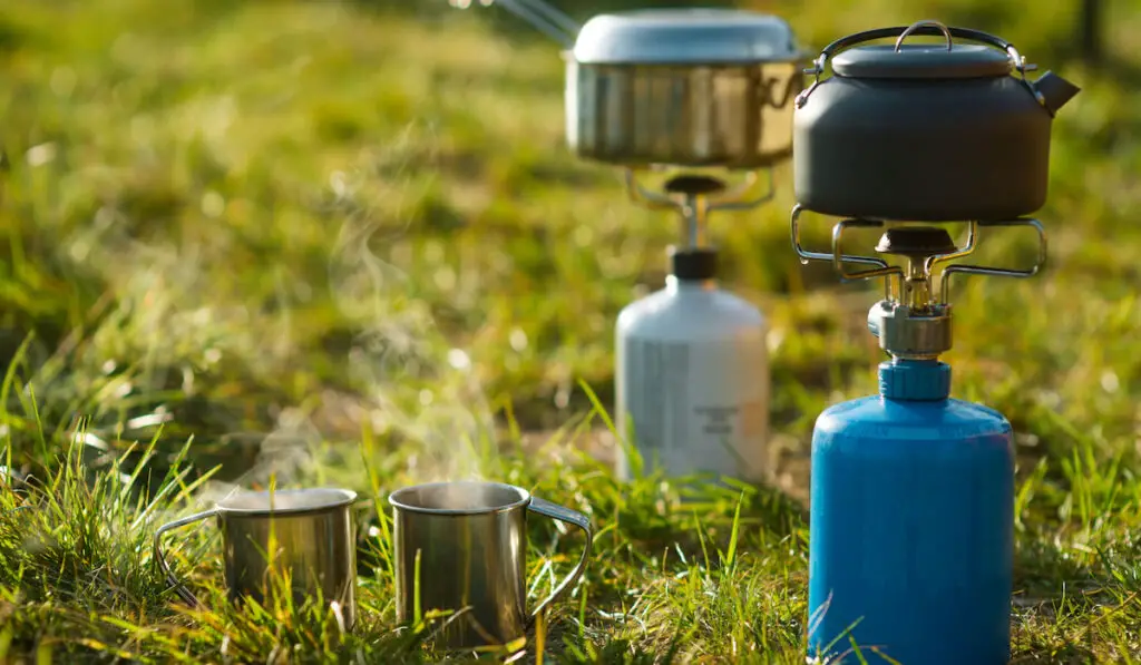 Metal mugs and kettle on portative gas stove for camping