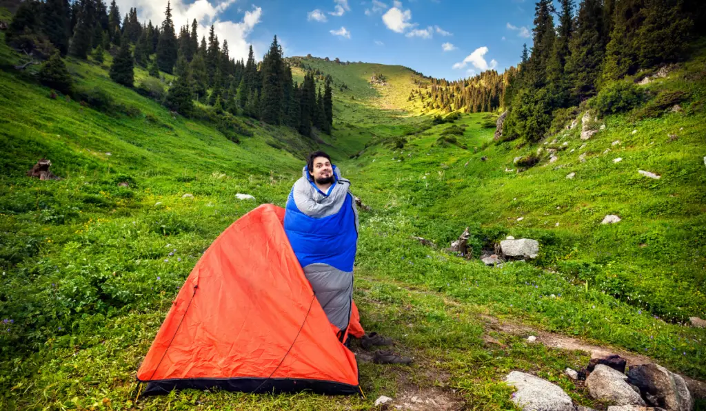 Tourist in sleeping bag near orange tent