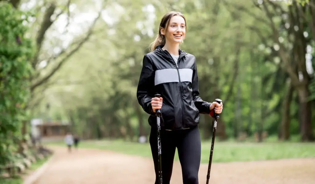 Young woman in black sportswear walking with hiking sticks in the park