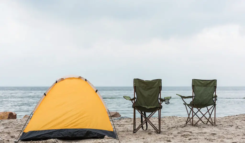 camping tent with two chairs standing on seashore
