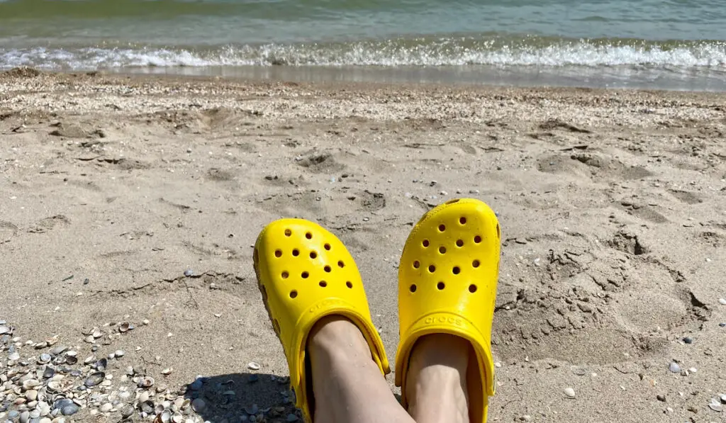cropped photo of woman wearing Bright yellow crocs on the beach 