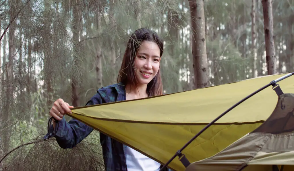 woman checking tent while camping in forest on summer time 
