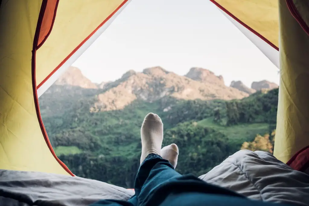 woman lying down and cross leg on blanket in tent and looking at mountain