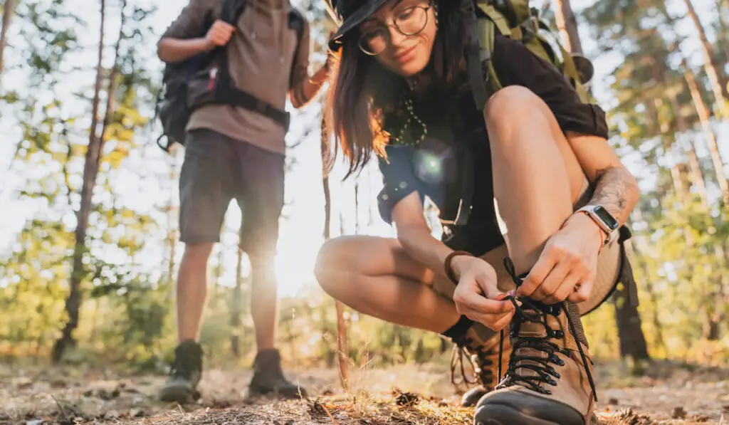 woman tying hiking boot outdoors on trail in forest 