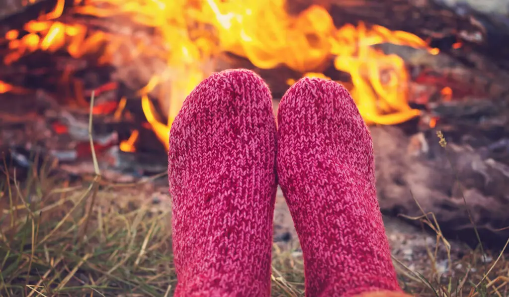 woman warming her feet wearing socks near campfire on camping