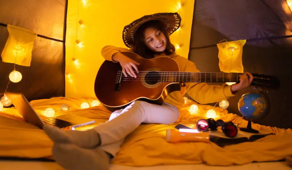 Little girl playing acoustic guitar under the tent