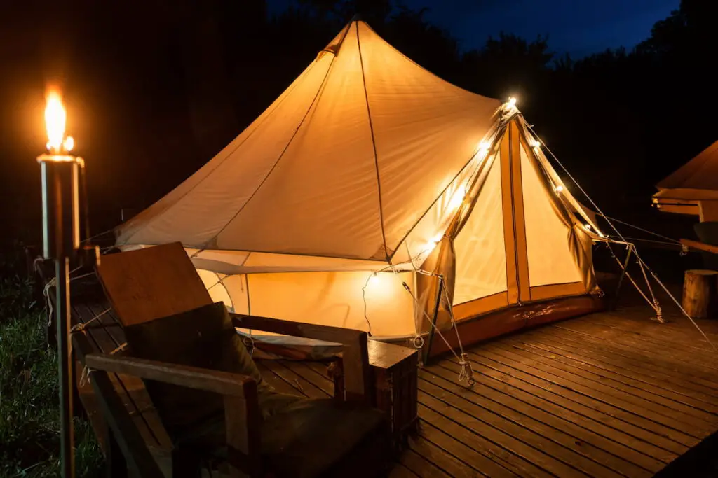 Tent with burning torch, lamps and wooden chair at glamping