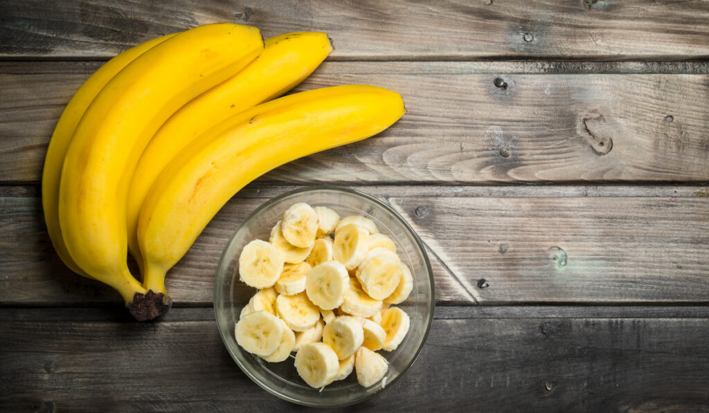 Fresh bananas and banana slices in a glass bowl on wooden table