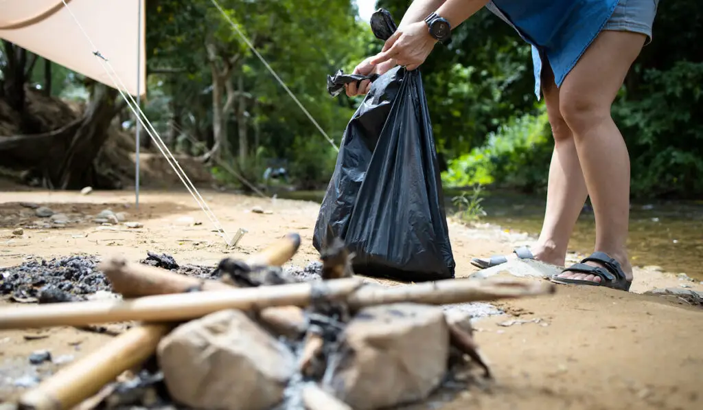 Woman collecting litter with gatbag bag after camping in the forest